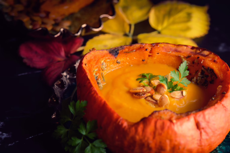 Rich pumpkin soup served in an edible pumpkin bowl with fall leaves.