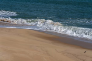 A serene scene of waves gently crashing onto a sandy beach under the daytime sun.