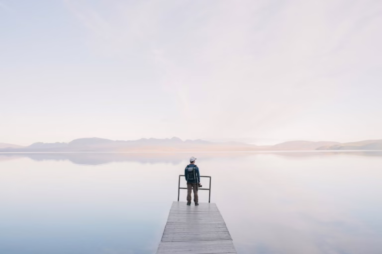 A solitary traveler stands on a dock enjoying the serene water view