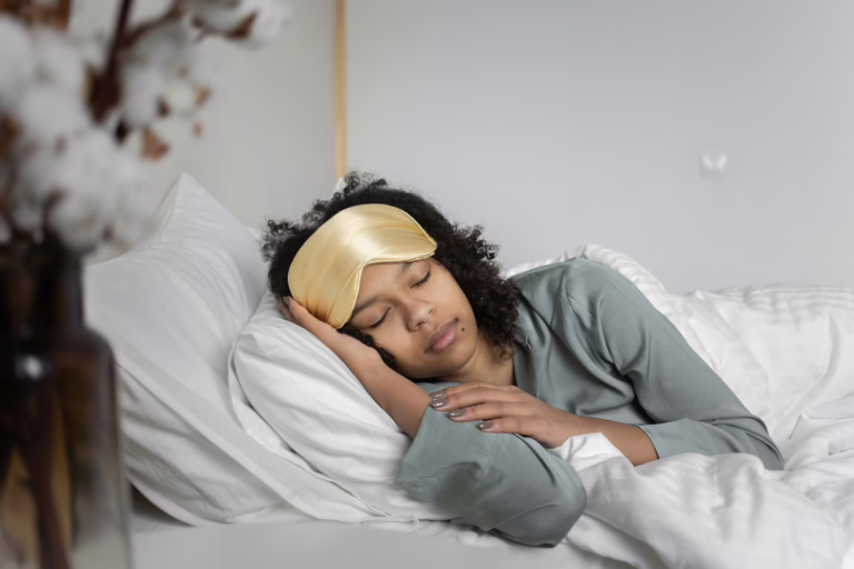 A young woman peacefully sleeps with a sleep mask, nestled in cozy white bedding.