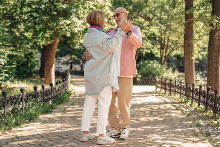 A joyful elderly couple dancing outdoors, showcasing love and happiness in a sunlit park.