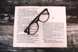 An open book with reading glasses placed on a rustic wooden table, inviting to read.